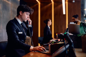 Hotel manager on the phone looking at a computer at the reception desk.