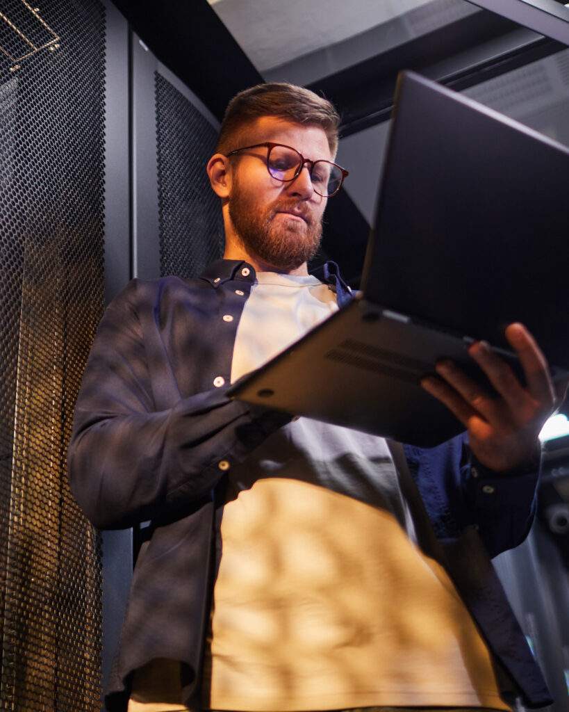Man working in server room and investigating on his laptop.