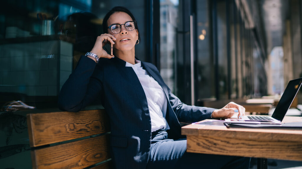 Businesswoman speaking on the phone outside at a table with a laptop.